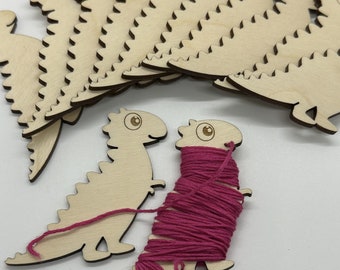 May include: Wooden dinosaur shaped yarn holders with pink yarn wrapped around one of the dinosaurs.