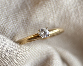 May include: A simple gold band ring with a single round diamond in the centre.