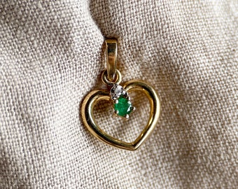 Puede incluir: Un colgante de corazón de oro con una esmeralda verde y dos diamantes más pequeños.