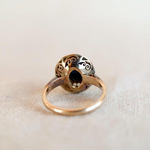 May include: A vintage gold ring with an oval, dark blue gemstone. The ring's setting features intricate filigree detailing around the gemstone. The band is a simple, polished gold. The ring is set against a neutral background.