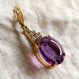 May include: A gold pendant with a large oval amethyst gemstone surrounded by smaller clear gemstones.
