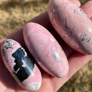Pu&ograve; includere: Tre pietre levigate di colore rosa e nero con una forma ovale liscia. Le pietre presentano un motivo a spirale di rosa e nero.