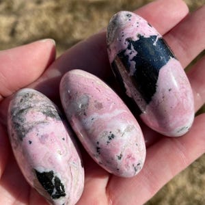 Pu&ograve; includere: Tre pietre levigate di colore rosa e nero. Le pietre sono lisce e lucidate, con una variet&agrave; di motivi rosa e neri.