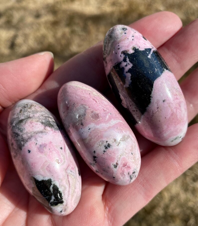 Pu&ograve; includere: Tre pietre levigate di colore rosa e nero. Le pietre sono lisce e lucidate, con una variet&agrave; di motivi rosa e neri.
