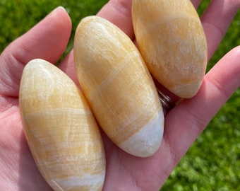 May include: Three yellow calcite egg-shaped stones with white striations. The stones are smooth and polished.