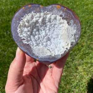 May include: A heart-shaped agate geode with a purple and white exterior and a white crystal interior. The geode is polished and has a smooth surface.
