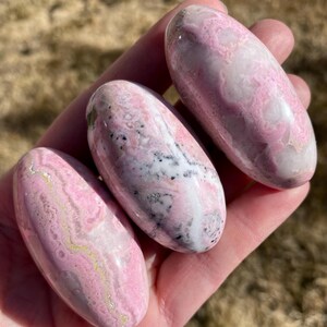 Pu&ograve; includere: Tre pietre levigate di colore rosa e bianco, di forma ovale e liscia. Le pietre presentano un motivo a spirale di rosa, bianco e grigio.