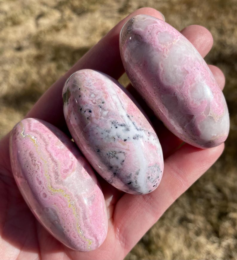 Pu&ograve; includere: Tre pietre levigate di colore rosa e bianco, di forma ovale e liscia. Le pietre presentano un motivo a spirale di rosa, bianco e grigio.