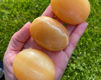 May include: Three smooth, yellow-orange, polished stones with white veins. The stones are oval shaped and have a glossy finish.