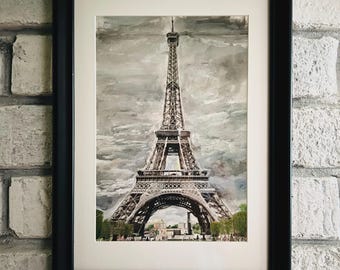 May include: Watercolor painting of the Eiffel Tower in Paris, France, framed in a black frame with a white mat. The artwork depicts the iconic tower against a cloudy, gray sky. The painting captures the architectural details of the tower.
