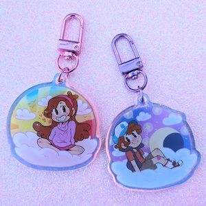 May include: Two round, clear acrylic keychains with colorful cartoon characters. The keychain on the left features a girl with brown hair wearing a pink sweater and sitting on a cloud. The keychain on the right features a boy with brown hair wearing a red and white shirt and sitting on a cloud. Both keychains have a silver metal clasp.