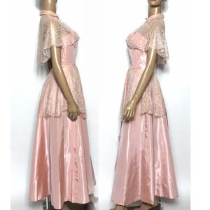 May include: A vintage pink satin and lace dress with a matching lace cape. The dress has a fitted bodice and a full skirt. The lace is delicate and has a floral pattern.