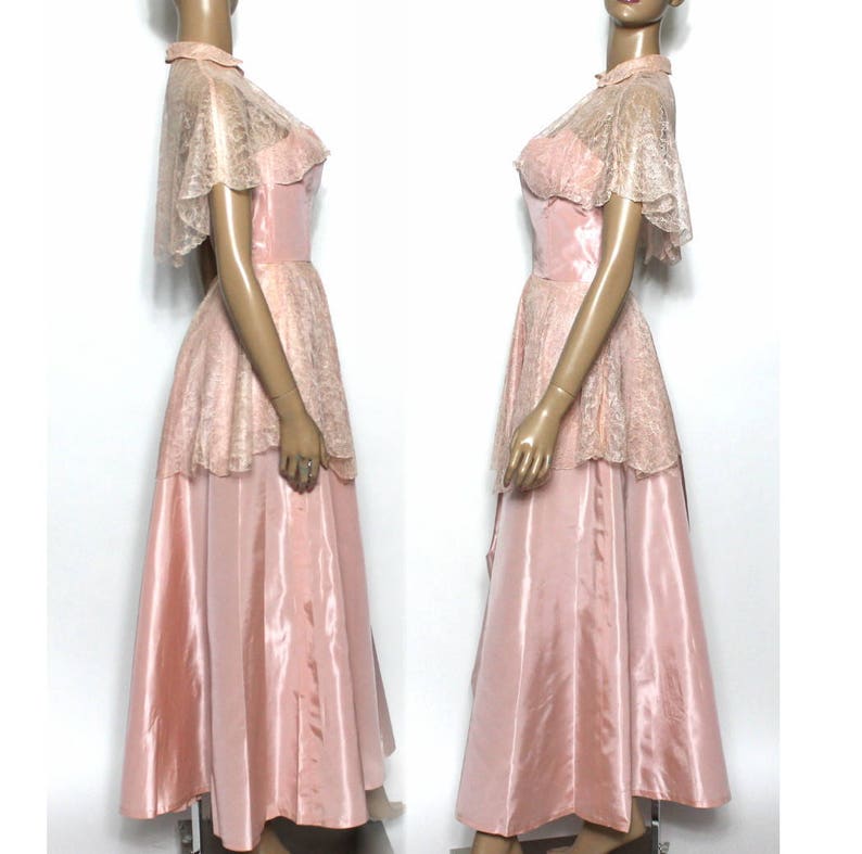 May include: A vintage pink satin and lace dress with a matching lace cape. The dress has a fitted bodice and a full skirt. The lace is delicate and has a floral pattern.