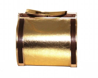 May include: A vintage gold handbag with a rectangular shape. The bag features a gold metallic exterior, dark brown wooden accents, and a matching gold handle. The bag has a boxy design with a clasp closure.