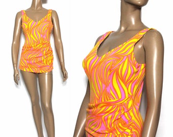 Op de afbeelding: Een vintage badpak uit één stuk met een levendig, abstract patroon. Het badpak heeft een V-hals en een gerimpeld detail aan de zijkant. Het ontwerp bevat wervelende lijnen in fel oranje, geel en roze, wat een opvallende look creëert.