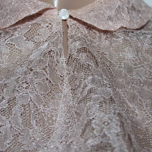 May include: A delicate, light pink lace blouse with a classic collar. The fabric is sheer and features a delicate floral pattern.