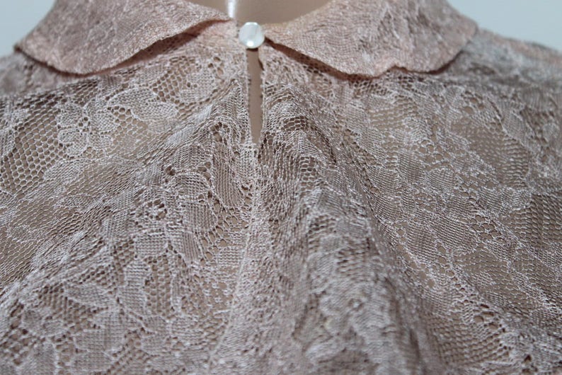 May include: A delicate, light pink lace blouse with a classic collar. The fabric is sheer and features a delicate floral pattern.