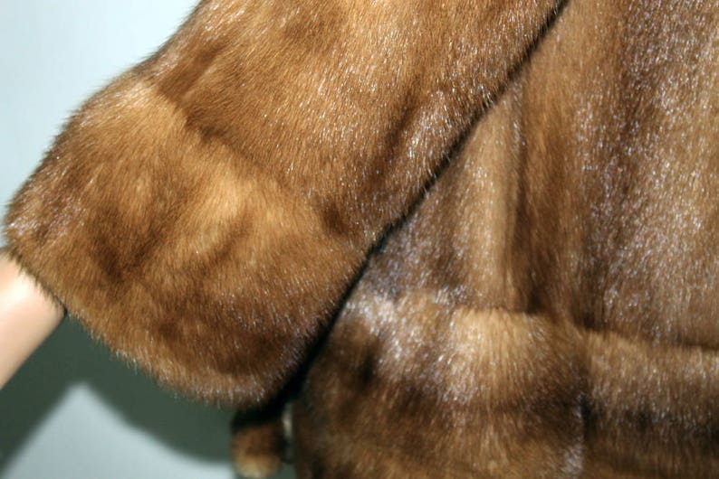K&ouml;nnte beinhalten: Eine braune Pelzjacke mit langem &Auml;rmel und breitem B&uuml;ndchen. Das Fell ist weich und flauschig.