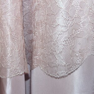 May include: Close-up of a delicate, off-white lace fabric with a floral pattern. The lace is soft and flowing, with a subtle sheen.