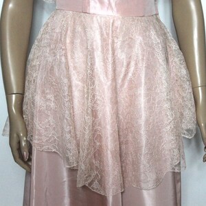 May include: A pink satin dress with a lace overlay. The lace is a delicate floral pattern and is layered over the satin skirt.