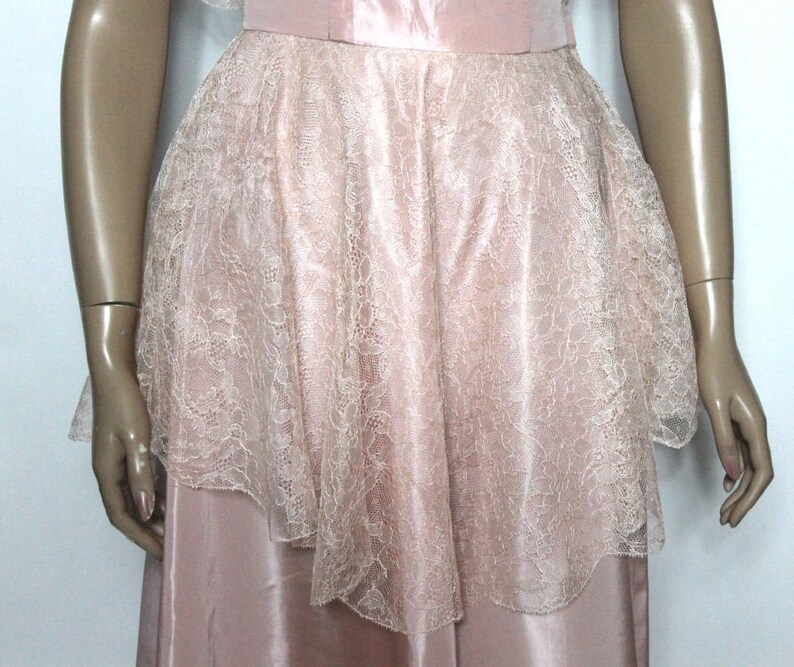 May include: A pink satin dress with a lace overlay. The lace is a delicate floral pattern and is layered over the satin skirt.