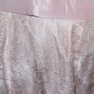 May include: A close-up of a light pink fabric with a delicate lace pattern. The lace is a lighter shade of pink and has a delicate floral design.