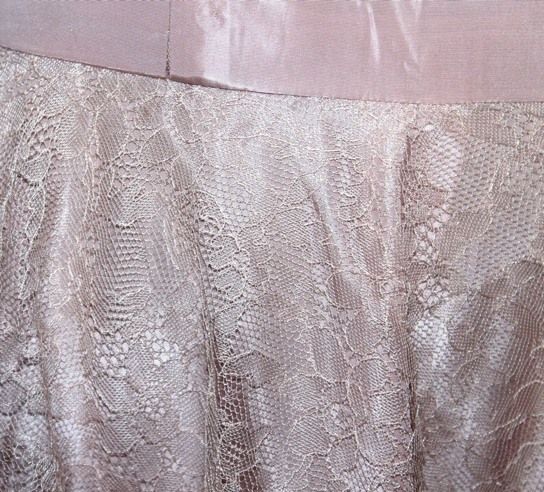 May include: A close-up of a light pink fabric with a delicate lace pattern. The lace is a lighter shade of pink and has a delicate floral design.