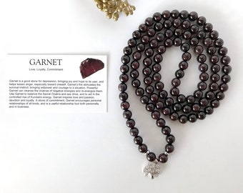 Può includere: Un mala di pietre preziose di granato rosso scuro con un ciondolo ad albero della vita argentato. Il mala è composto da 108 perle ed è utilizzato per la meditazione e la preghiera. La carta nell'immagine recita "Granato Amore, Lealtà, Impegno".