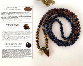Può includere: Una collana a strati con perline marroni, blu e oro. La collana ha un ciondolo con una pietra occhio di tigre triangolare e un piccolo ciondolo. Le schede informative descrivono le proprietà di Occhio di Tigre Rosso, Occhio di Tigre e Occhio di Tigre Blu.