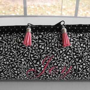 May include: A black and white floral print bag with pink accents. The bag features a black polka dot trim and pink tassels. The word "Joy" is embroidered in pink on the front. The bag has black handles with pink stripes.