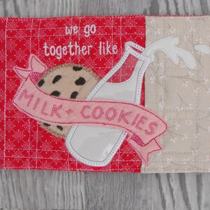 May include: A pink and white embroidered kitchen towel with a milk bottle and cookie design. The text "we go together like milk + cookies" is embroidered on the towel.