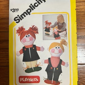 May include: Simplicity sewing pattern number 6014 for making two Playskool dolls. The pattern includes instructions for making a girl doll with red hair and a boy doll with blonde hair. The dolls are wearing clothes with a vintage style.