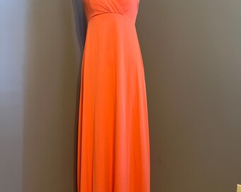 May include: A long, coral-colored halter dress with a simple, elegant design. The dress has a fitted bodice and a flowing skirt.