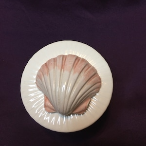 May include: A white ceramic trinket box with a pink and white seashell design on the lid.