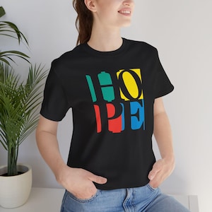 May include: Black t-shirt with the word "HOPE" in colorful block letters. The letters are teal, yellow, red, and blue. The shirt is a crew neck and made of a soft material.