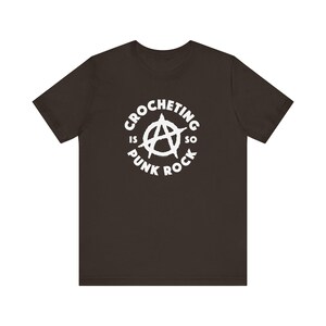 May include: A dark brown t-shirt with a white circle graphic that says "Crocheting is so punk rock" with an anarchy symbol in the center.