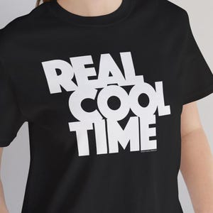 以下が含まれることがあります： 「REAL COOL TIME」という白い文字が書かれた黒いTシャツです。