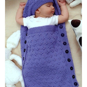 May include: A purple knitted baby sleeping bag with a matching hat. The sleeping bag has a row of buttons down the side.