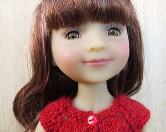 May include: A red knitted cardigan with short sleeves and three red buttons. The cardigan is worn by a doll with long brown hair and bangs.