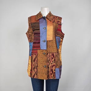 May include: A patchwork vest with a collared neckline and button-down front. The vest features a variety of patterned fabrics in shades of brown, orange, blue, and red. The vest is sleeveless and appears to be made of a quilted material.