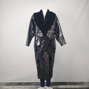May include: A long, black coat with a glossy finish and a plush, dark collar. The coat features a unique embossed pattern and a button closure. The coat is displayed on a mannequin, showcasing its full length and design.