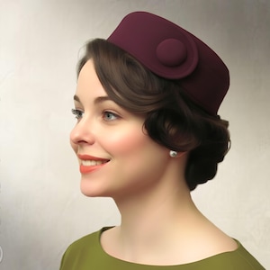 Puede incluir: Un sombrero cloche burdeos con un detalle de botón circular. El sombrero lo lleva una persona con cabello oscuro y una blusa verde. Las palabras "Elschen Sewing Pattern" y "Instant PDF Download" están impresas en la imagen.