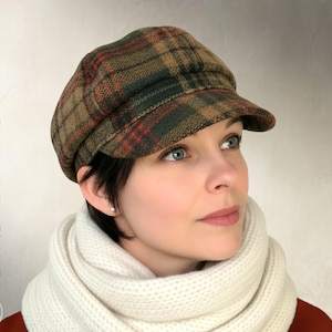 Op de afbeelding: Een geruite newsboy-pet in bruin, groen en rood. Het model draagt een witte sjaal en een rode top. De tekst links zegt "Elsewhen Sewing Pattern" en de tekst rechts zegt "Instant PDF Download".