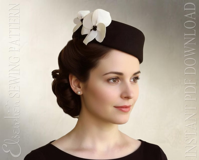 May include: A black pillbox hat adorned with two white orchid-like flowers featuring dark centers. The text "Elsewchen SEWING PATTERN" and "INSTANT PDF DOWNLOAD" is visible on the sides of the image. The hat has a structured, rounded shape.