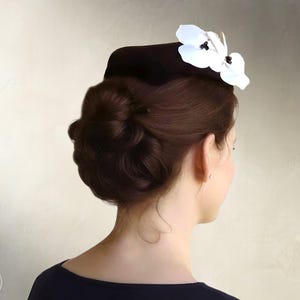 May include: A dark brown pillbox hat adorned with two white orchid-like flowers featuring dark centers. The text "Elsewchen SEWING PATTERN" and "INSTANT PDF DOWNLOAD" is visible on the left and right sides of the image respectively.