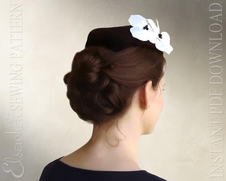 May include: A dark brown pillbox hat adorned with two white orchid-like flowers featuring dark centers. The text "Elsewchen SEWING PATTERN" and "INSTANT PDF DOWNLOAD" is visible on the left and right sides of the image respectively.