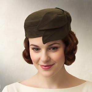 May include: A dark olive green pillbox hat featuring a structured crown and a decorative bow detail on the side. The text "Elsewhens SEWING PATTERN" and "INSTANT PDF DOWNLOAD" is visible on the left and right sides of the image respectively.