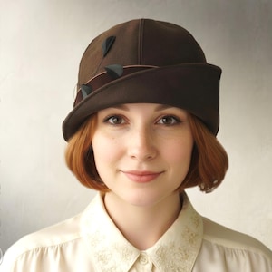 Puede incluir: Un sombrero cloche marrón oscuro con ala curvada y detalles decorativos. La persona lleva una blusa color crema. Las palabras "INSTANT PDF DOWNLOAD" están impresas verticalmente en el lado derecho de la imagen.