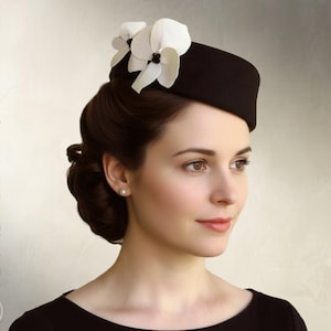 May include: A black pillbox hat adorned with two white orchid-like flowers featuring dark centers. The text "Elsewchen SEWING PATTERN" and "INSTANT PDF DOWNLOAD" is visible on the left and right sides of the image respectively.