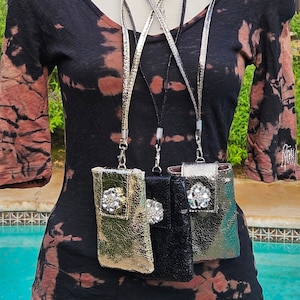 May include: Three cell phone pouches with rhinestones and a metallic finish. The pouches are hanging from black and silver lanyards. The pouches are gold, black, and silver.